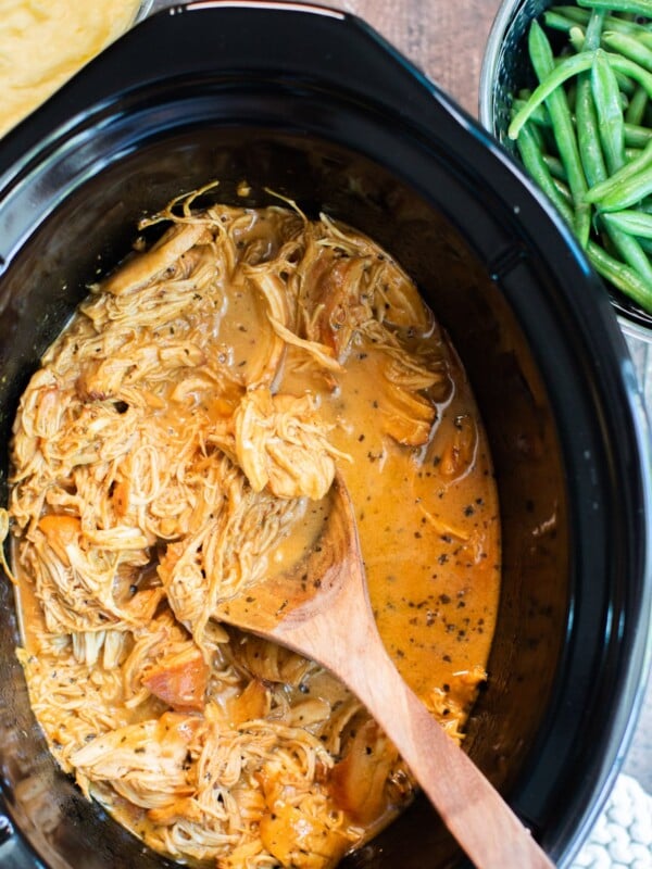 close up of shredded honey mustard chicken in slow cooker with green beans on the side.