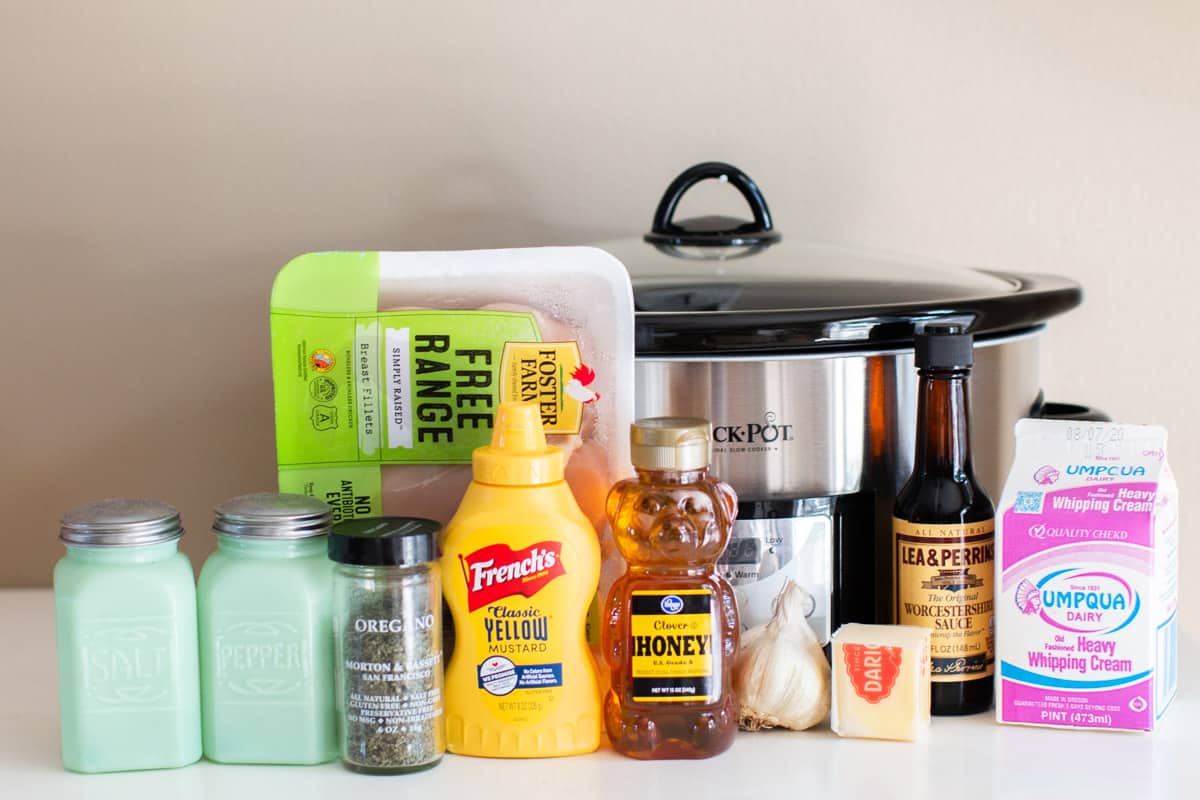 seasonings, chicken, mustard, honey, butter, worcestershire sauce and heavy whipping cream in front of a slow cooker.