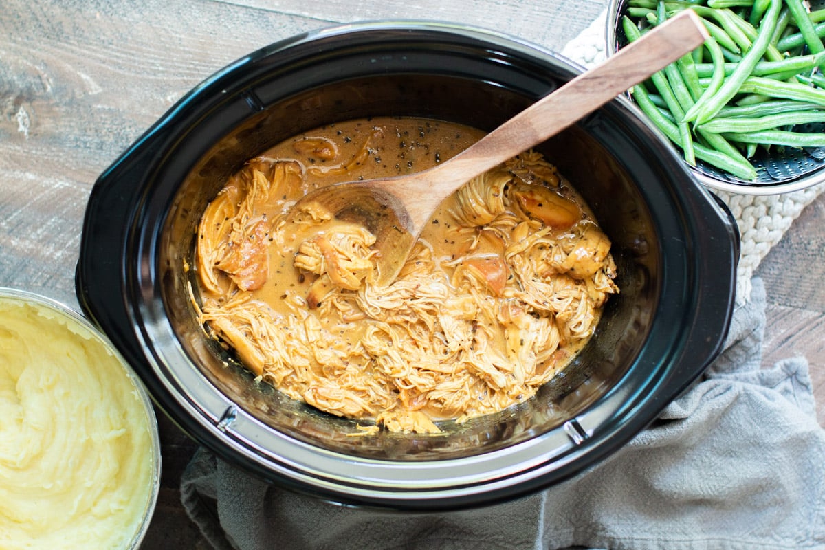 finished cooking honey mustard chicken in slow cooker with wooden spoon in it.