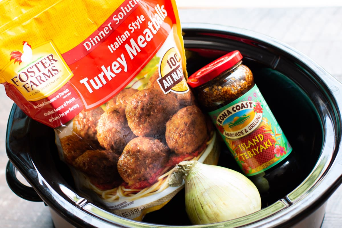 bag of frozen meatballs, jar of island teriyaki and an onion in a slow cooker