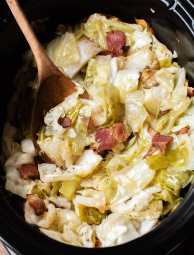 cabbage and bacon in slow cooker with a wooden spoon