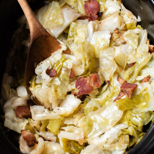 cabbage and bacon in slow cooker with a wooden spoon