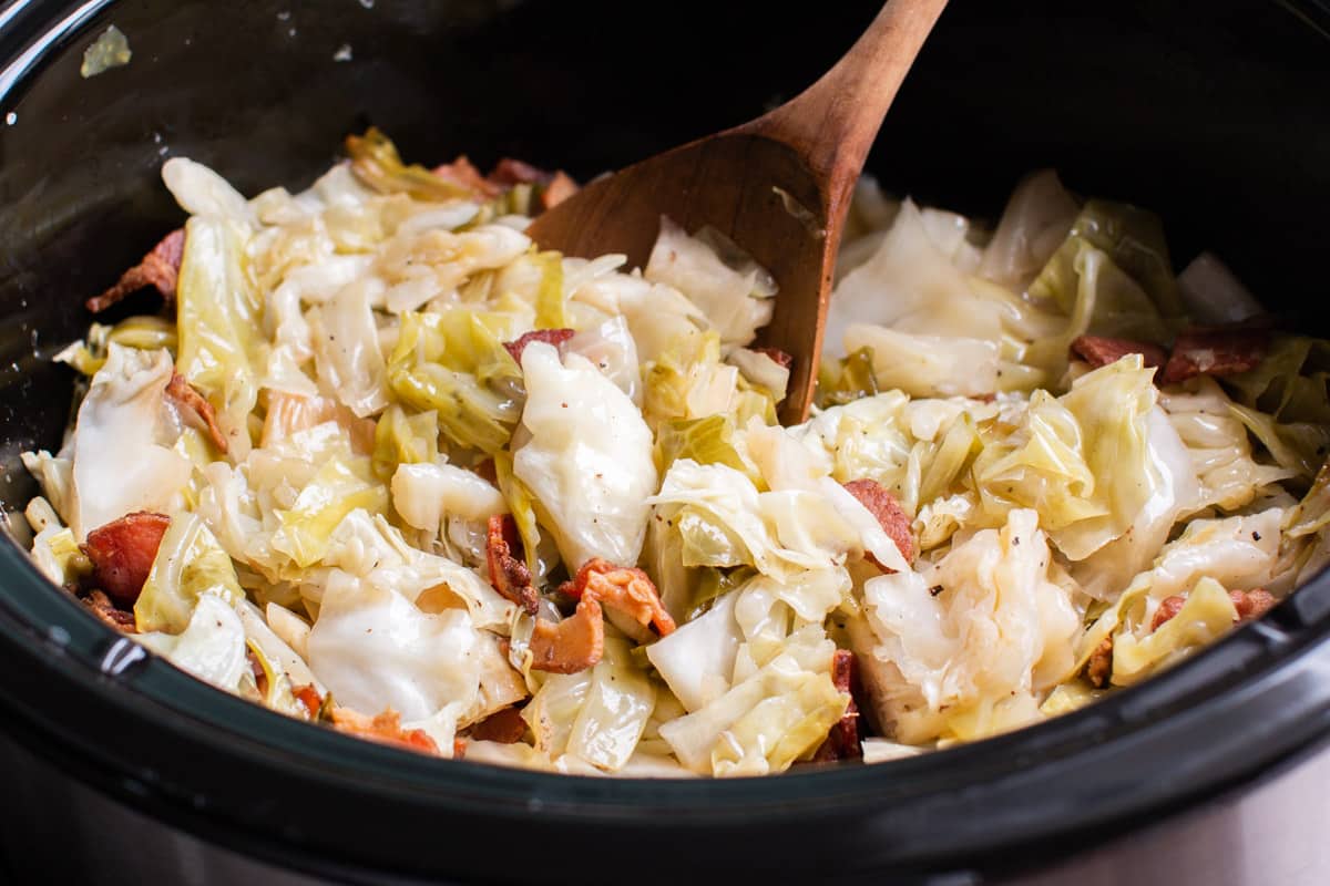 close up of cooked cabbage in slow cooker with wooden spoon in it.