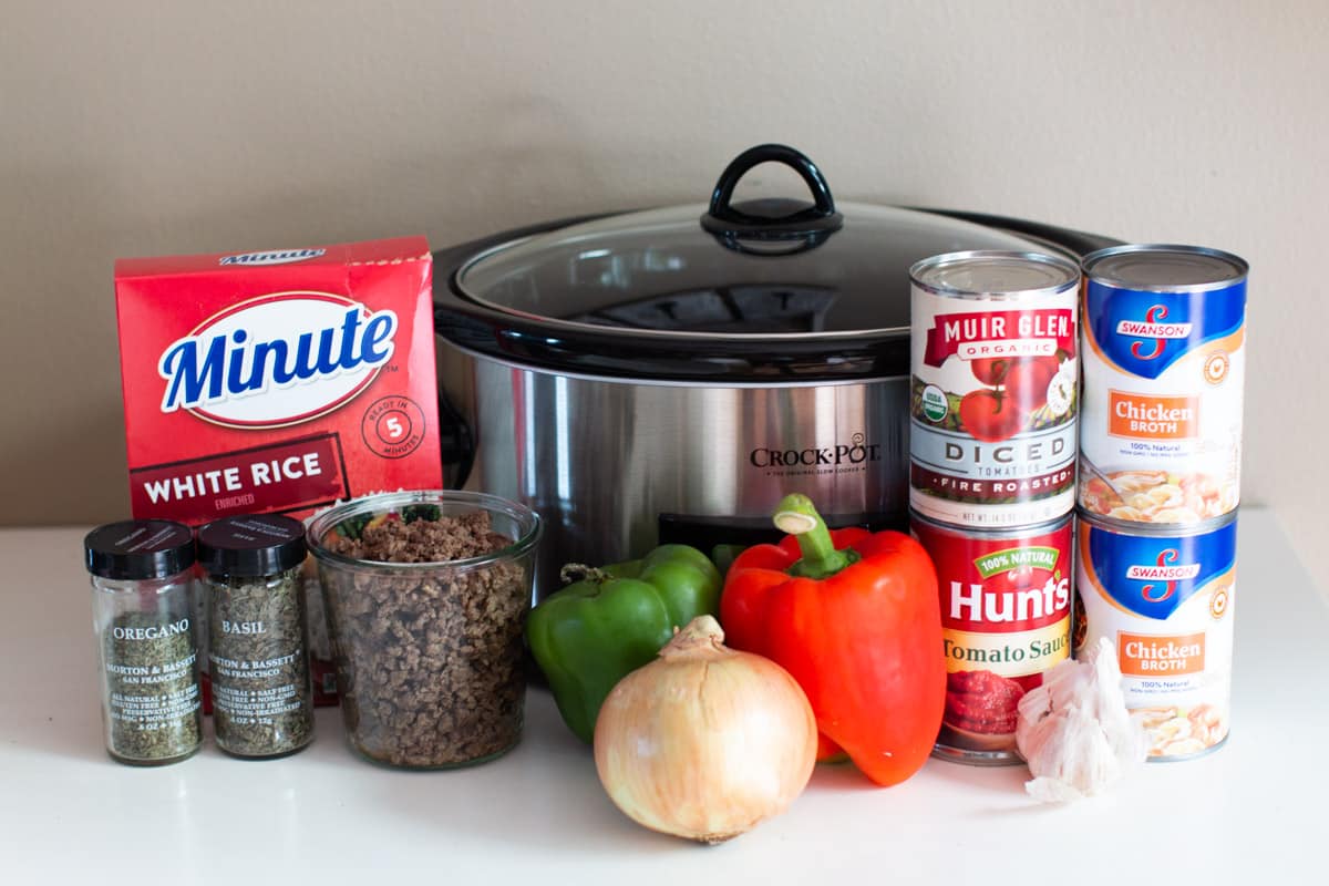 Cans of food, vegetables, minute rice, beef and seasonings in front of a slow cooker