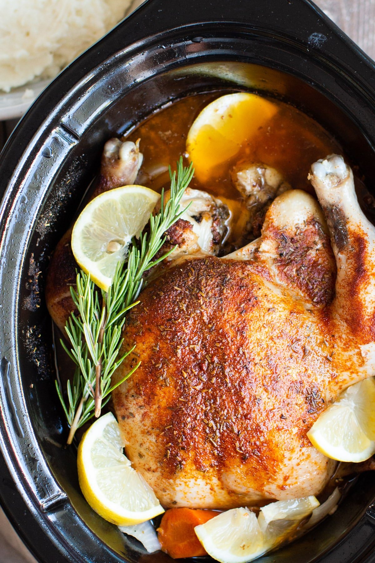 close up of a cooked whole chicken with lemon and rosemary in a slow cooker