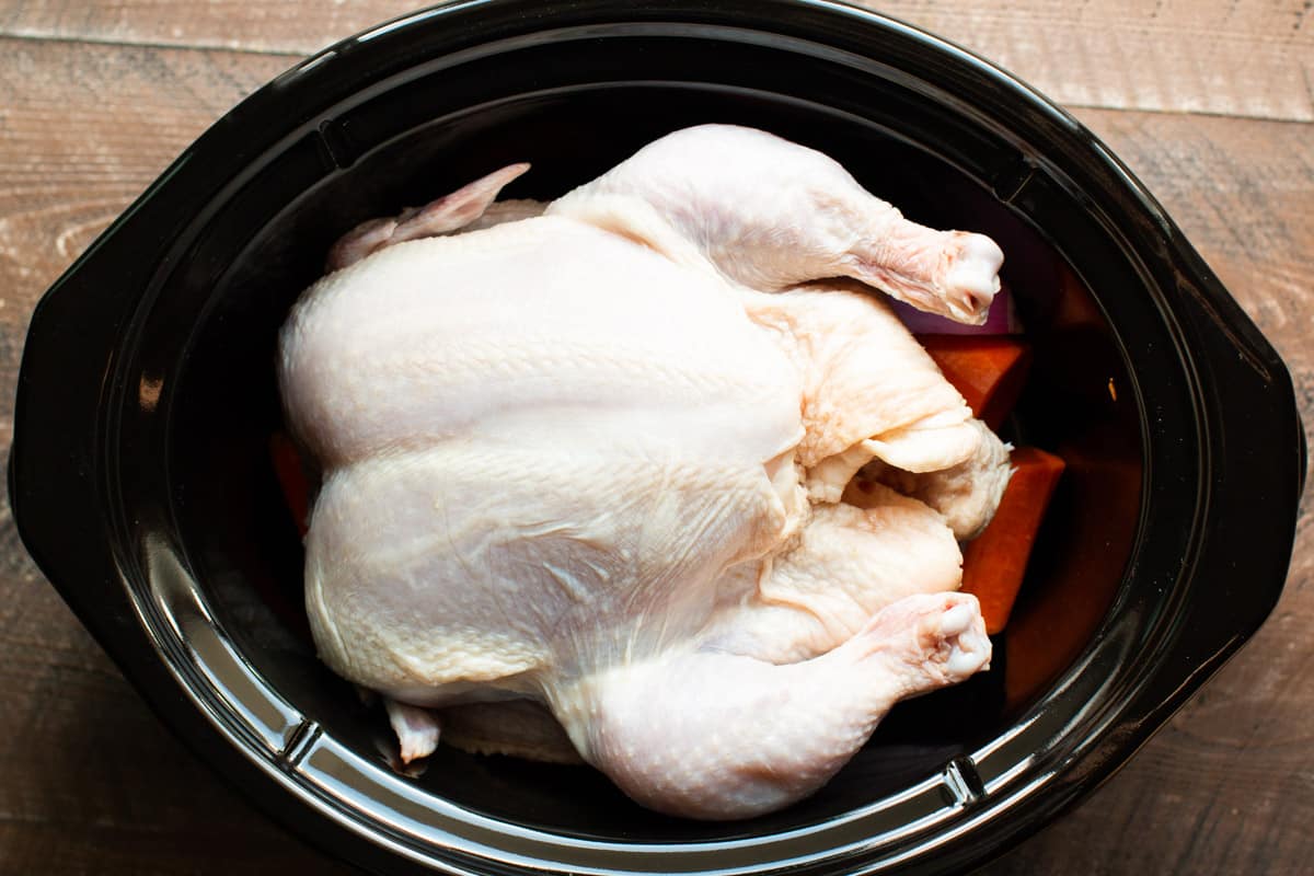 whole chicken on top of vegetables in a slow cooker.