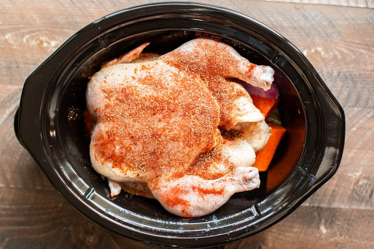 seasonings on top of a whole chicken in a slow cooker.