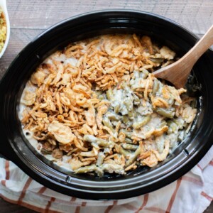 green bean casserole in a slow cooker with wooden spoon in it.