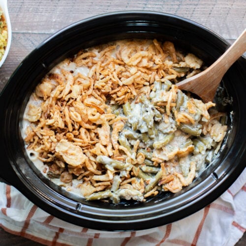 green bean casserole in a slow cooker with wooden spoon in it.