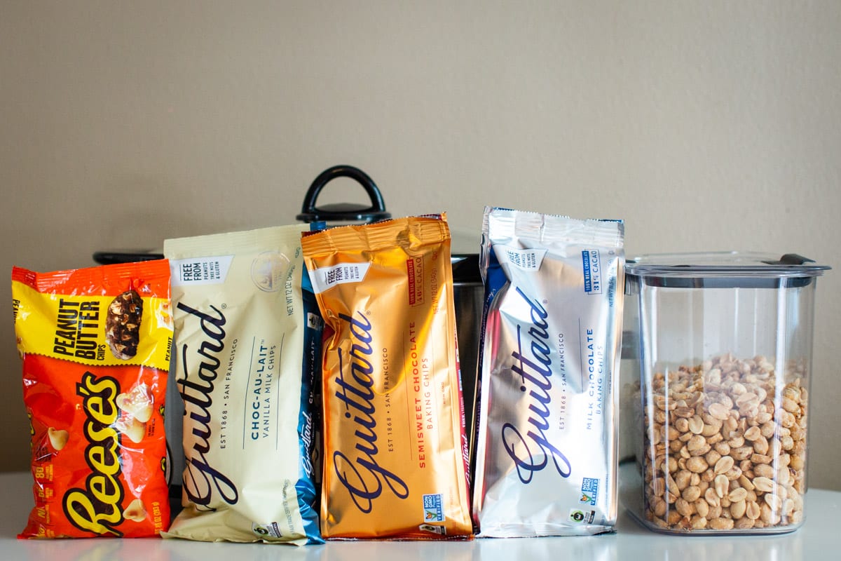 chocolate and peanut chips and peanuts in front of a slow cooker