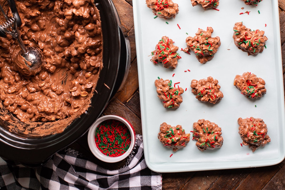 slow cooker with peanuts and chocolate and sheet pan of clusters