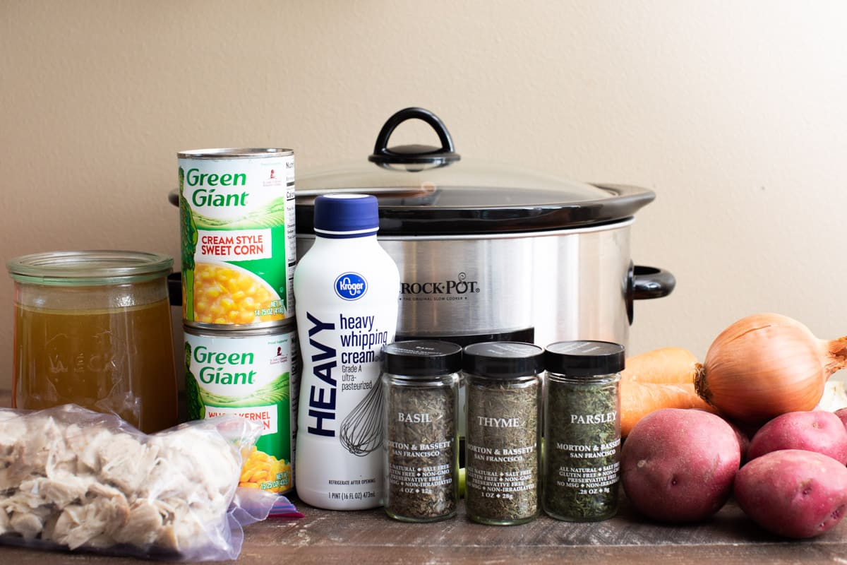 corn, spices, vegetables, cream, turkey broth, and turkey in front of the slow cooker.