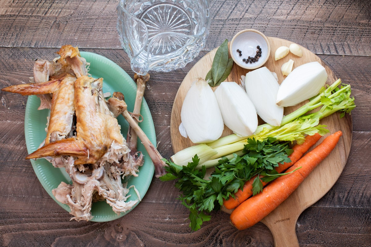 turkey pieces, vegetables, bay leaves, peppercorns and water on a table.