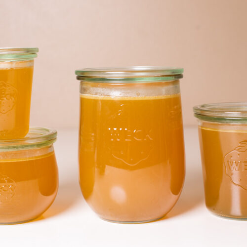 4 jars of turkey stock on a white table.