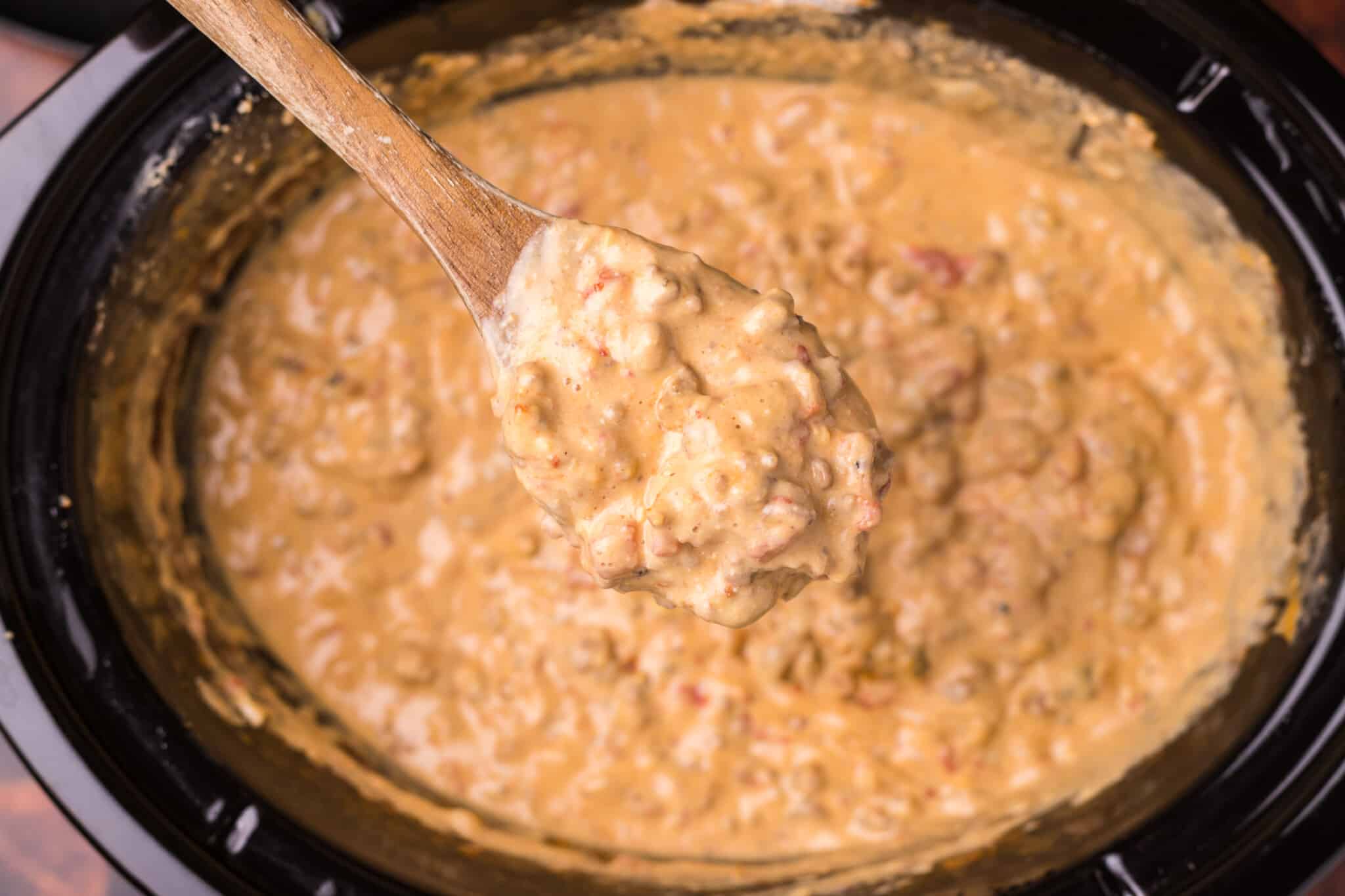 bacon cheeseburger dip on wooden spoon coming from a slow cooker