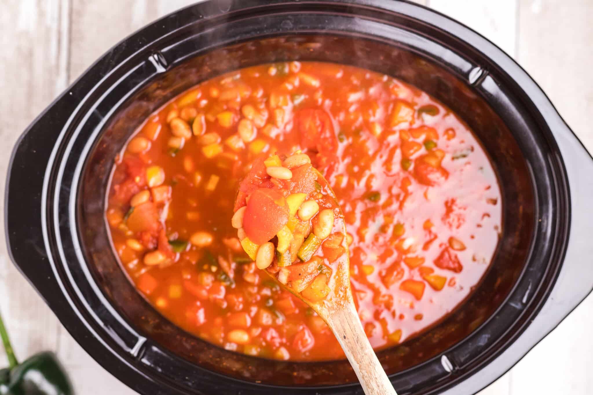 cooked vegetarian chili in slow cooker and on wooden spoon.