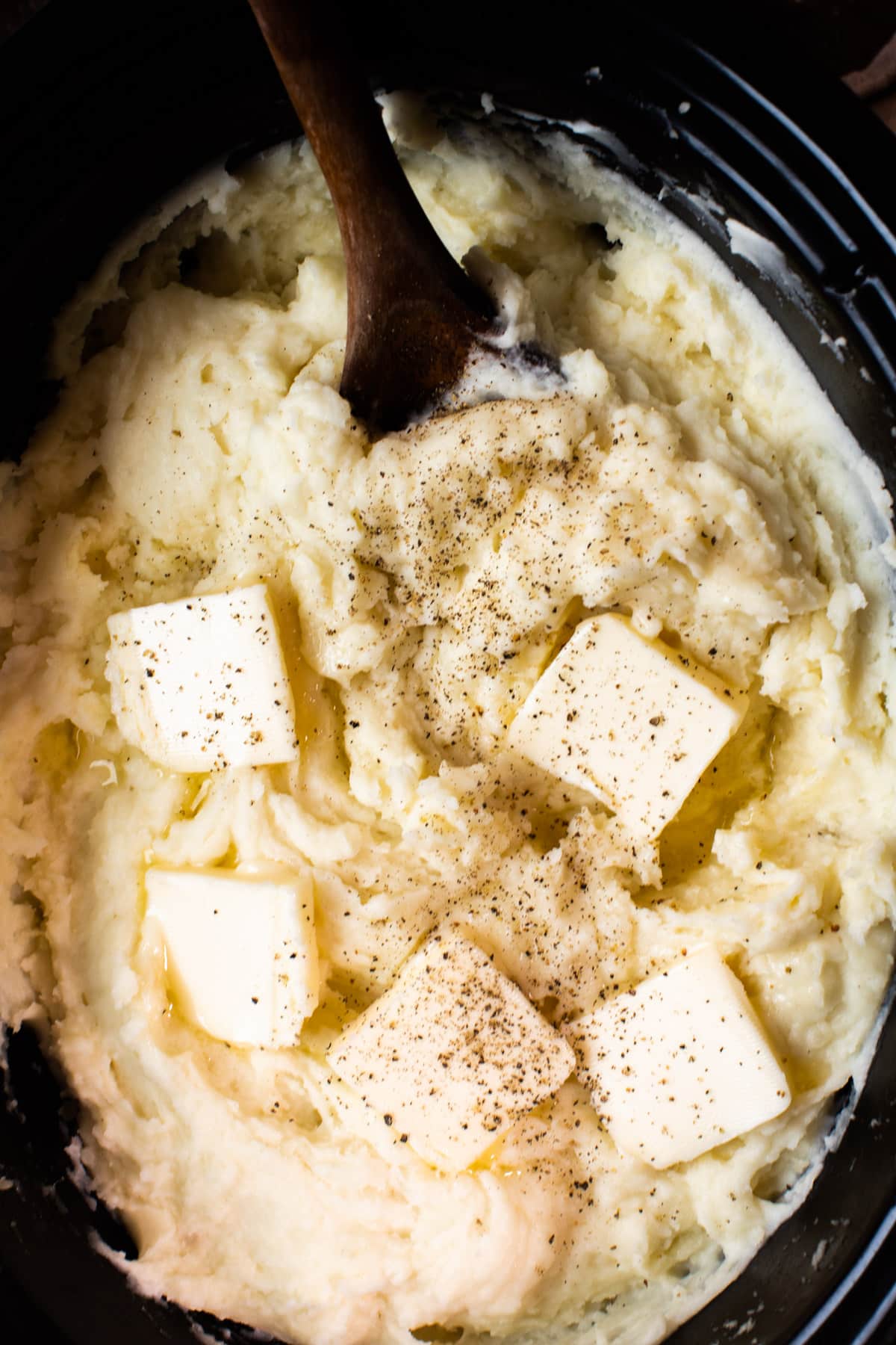 close up of mashed potatoes in a slow cooker with butter pats on top.
