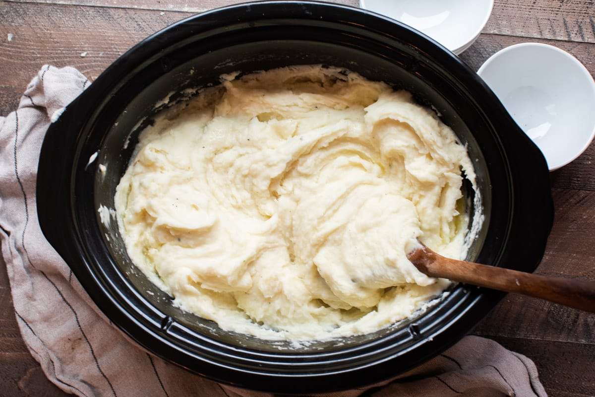 mashed potatoes in slow cooker with wooden spoon in them.