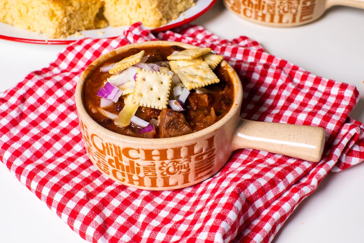 bowl of prime rib chili with crackers, cheese and onions on top.