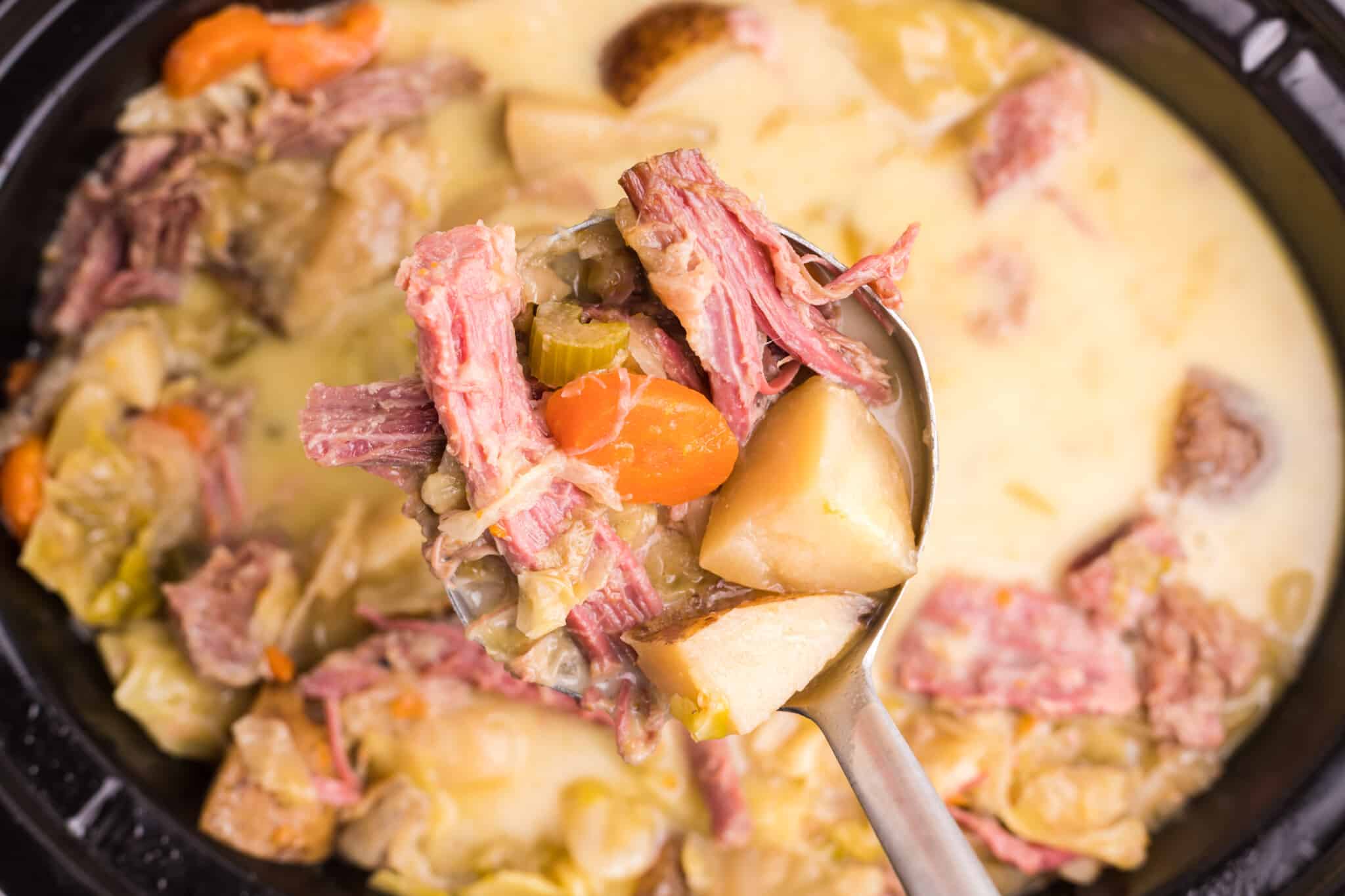 scoop of corned beef and cabbage soup coming from slow cooker