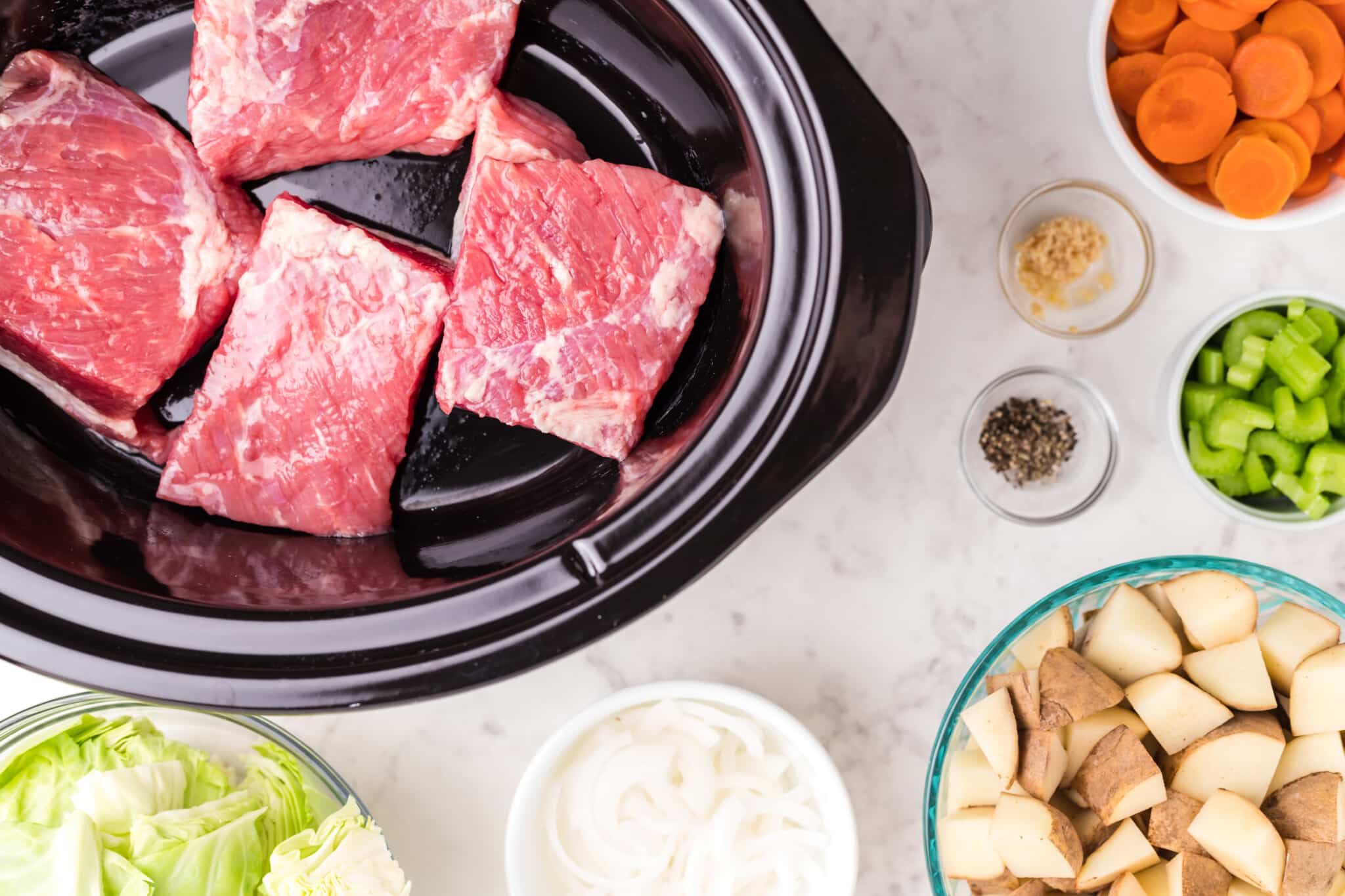 4 pieces of corned beef in slow cooker with veggies and spices on side