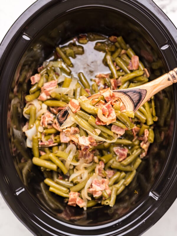 green beans and bacon is sauce in slow cooker and on wooden spoon