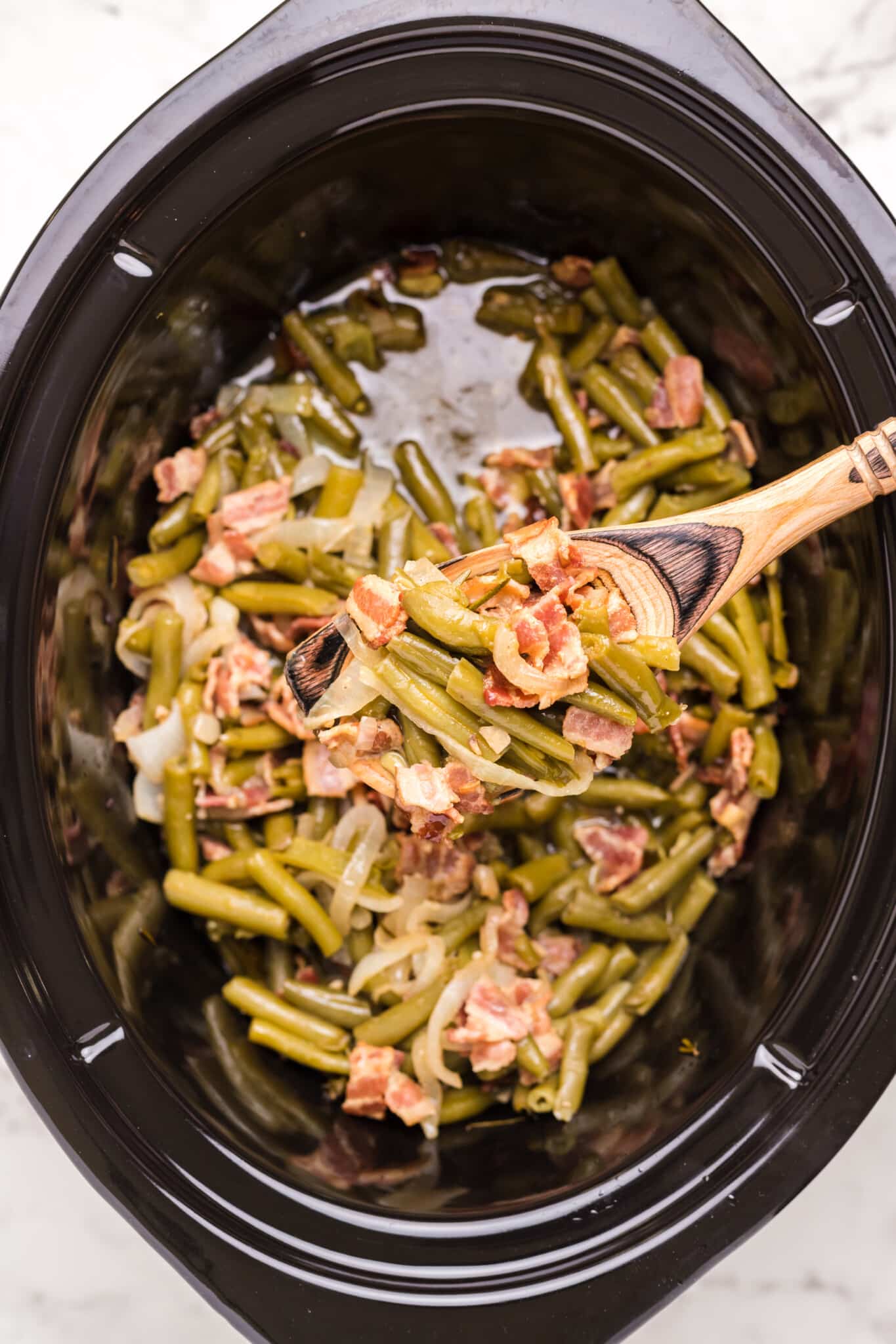 green beans and bacon is sauce in slow cooker and on wooden spoon