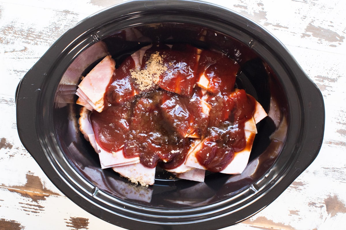 ham with barbecue sauce and brown sugar on top in slow cooker