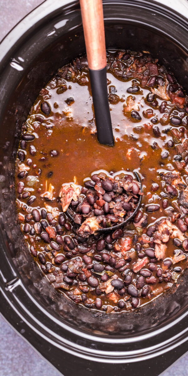 long image of black bean soup in slow cooker with ladle.