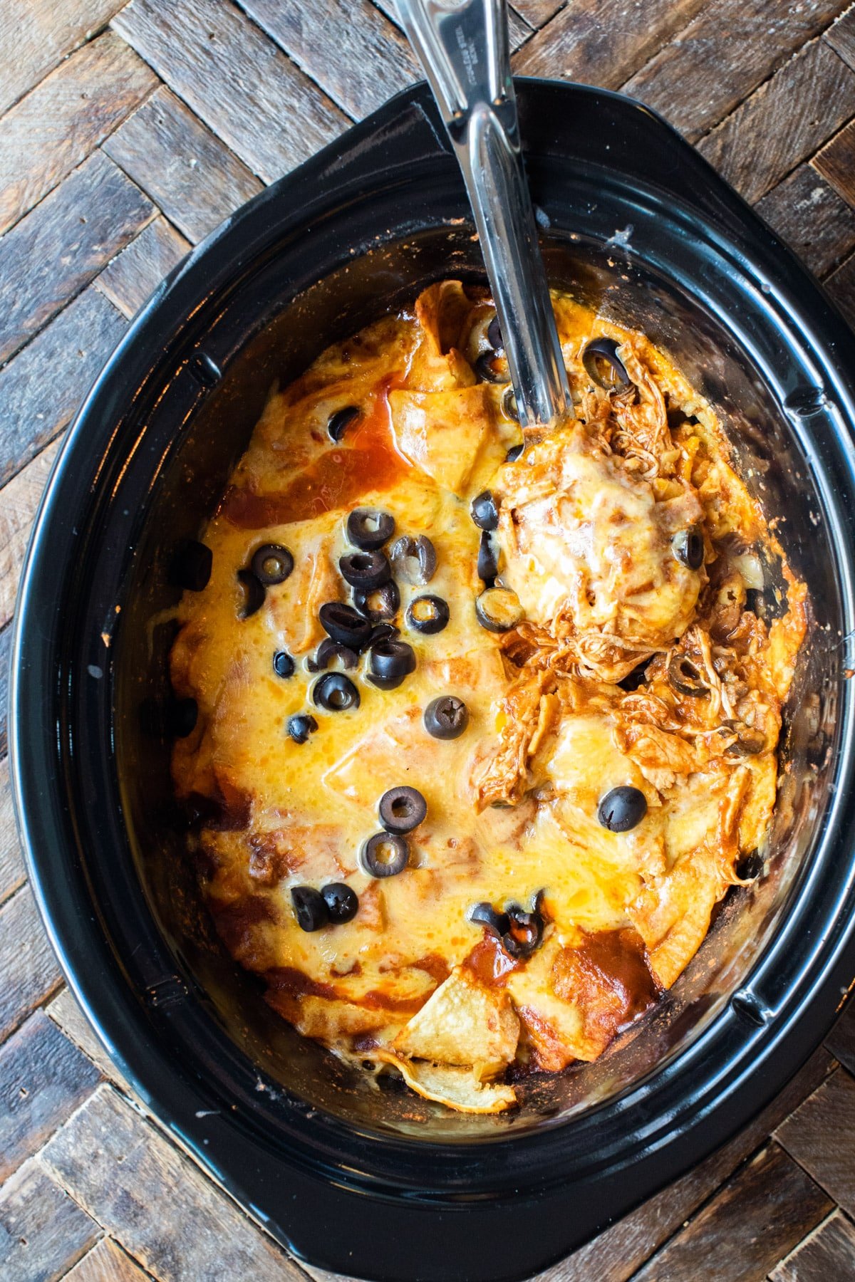 enchilada casserole with olives on top and metal spoon in it.