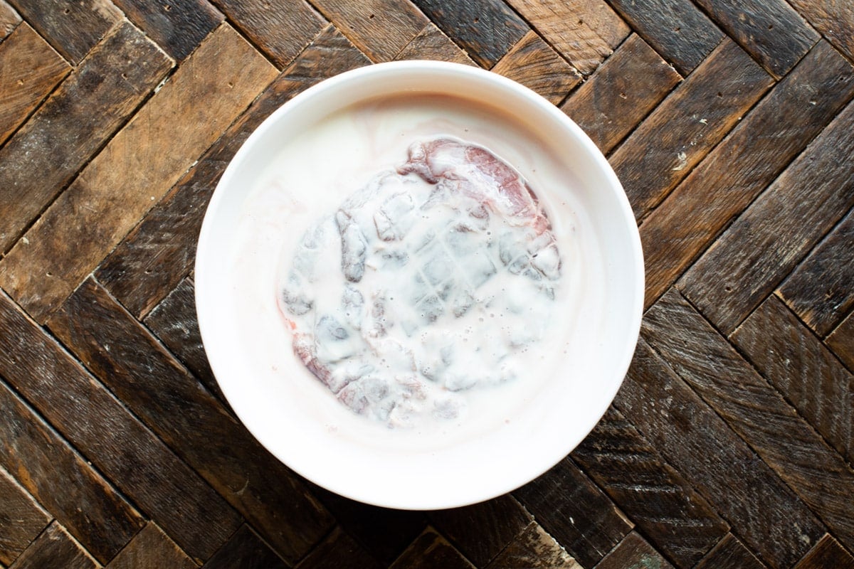 venison roast in a bowl, covered in buttermilk