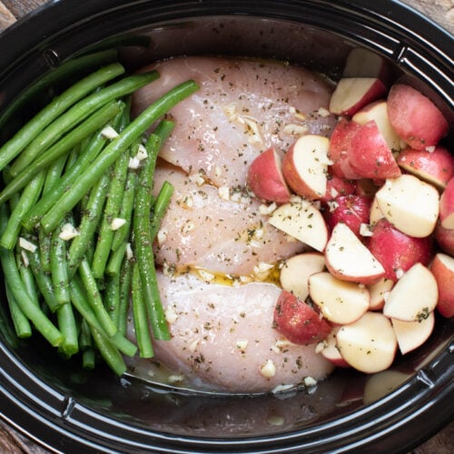 chicken, potatoes, green beans in slow cooker with dressing on top.