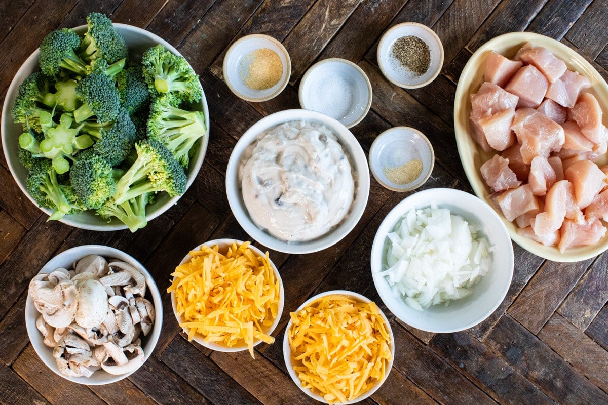 broccoli, cream of mushroom soup, mushrooms, onion, cheese and diced chicken on a table.