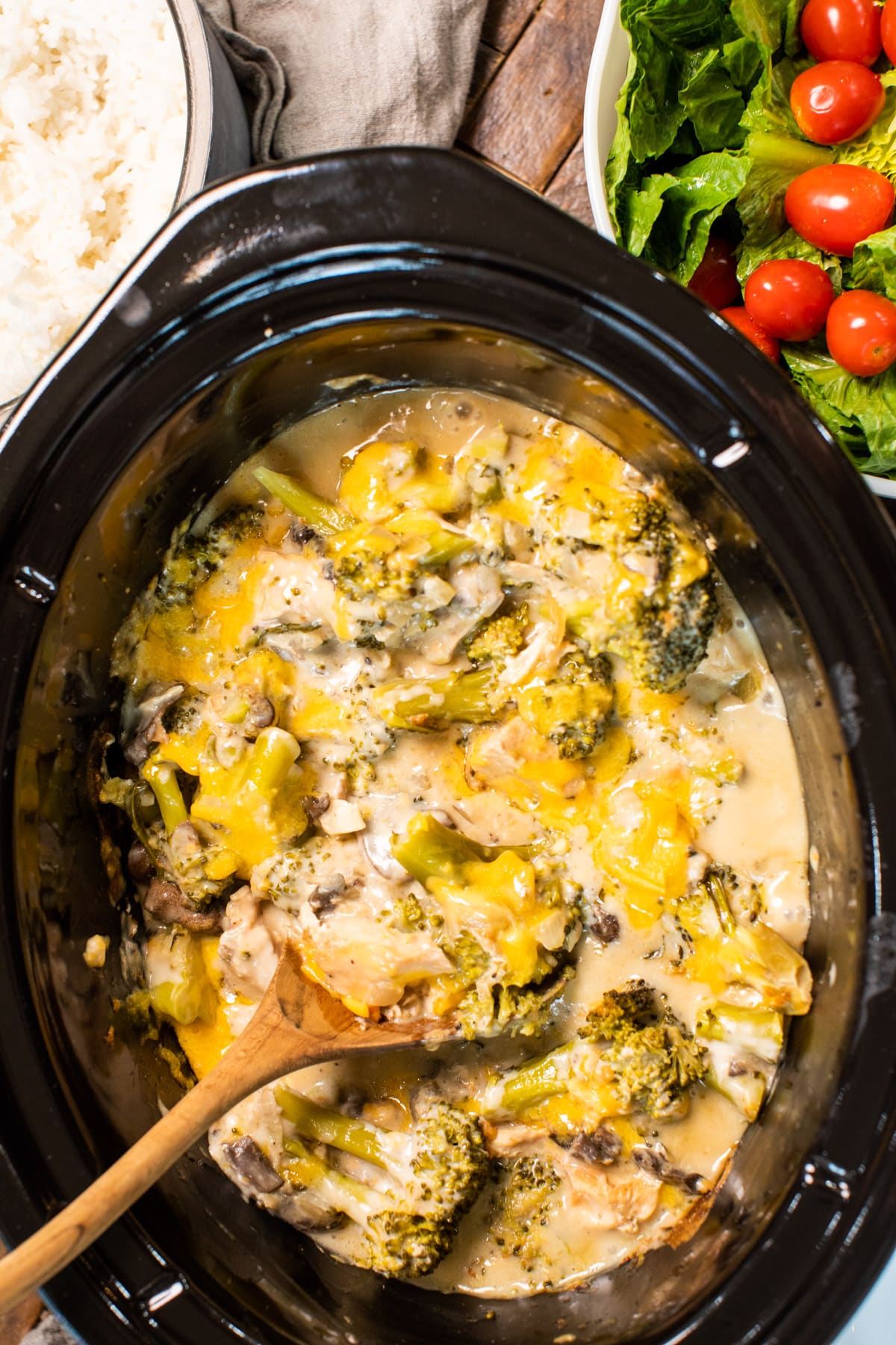 cheesy broccoli chicken in slow cooker with wooden spoon in it.