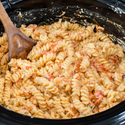 feta tomato pasta in slow cooker with wooden spoon in it