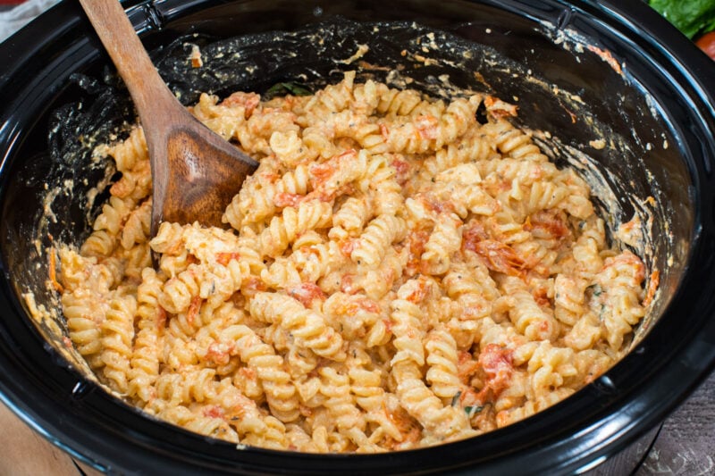 feta tomato pasta in slow cooker with wooden spoon in it