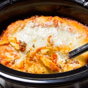 close up of ravioli in slow cooker with metal spoon in it.