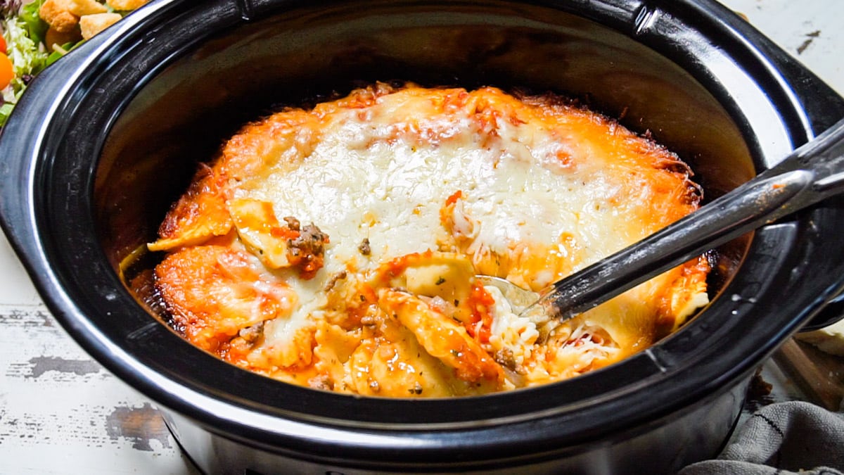 close up of ravioli in slow cooker with metal spoon in it.