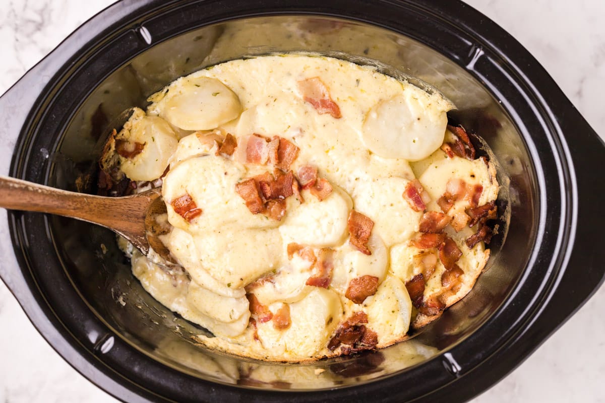 cooked scalloped potatoes with wooden spoon in it.