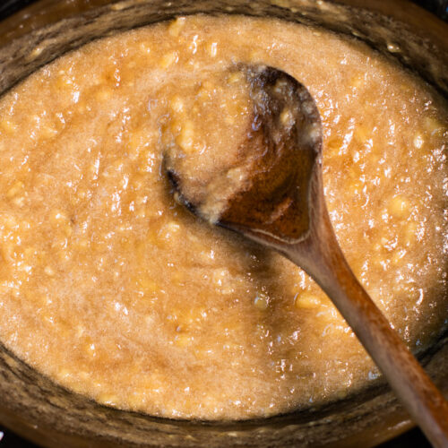 close up of banana jam in slow cooker with wooden spoon in it.