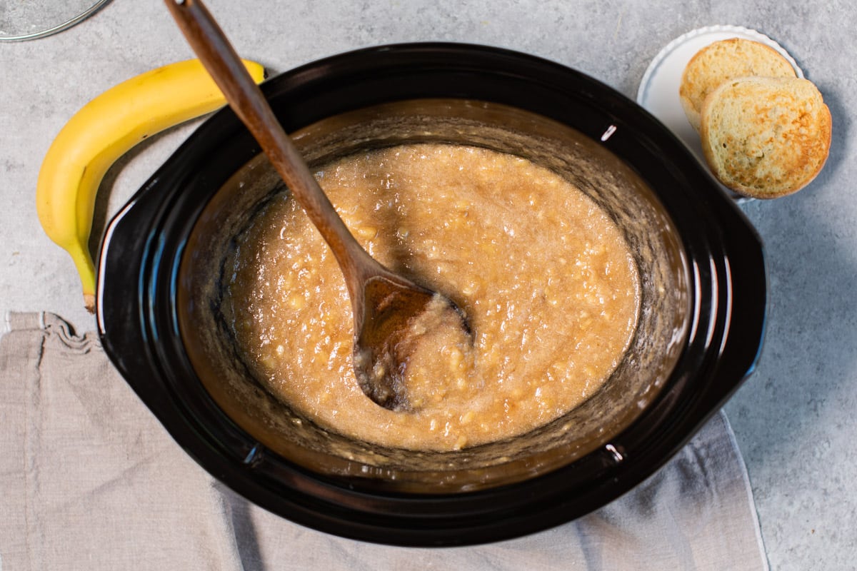 banana jam done cooking in slow cooker with wooden spoon in it