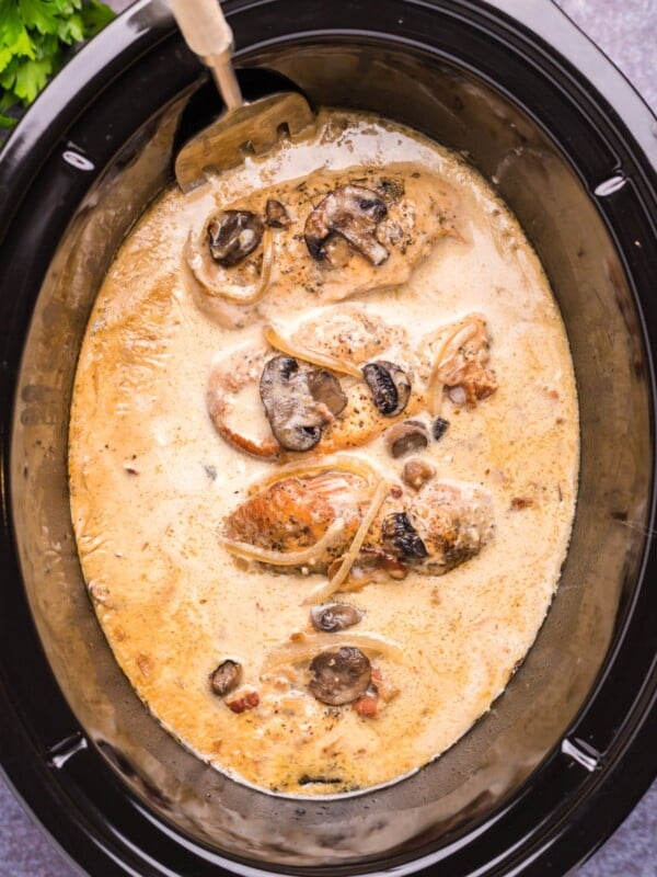close up of chicken marsala in slow cooker with spoon in it.