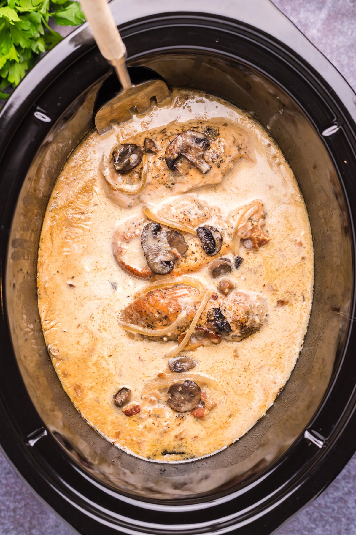 close up of chicken marsala in slow cooker with spoon in it.