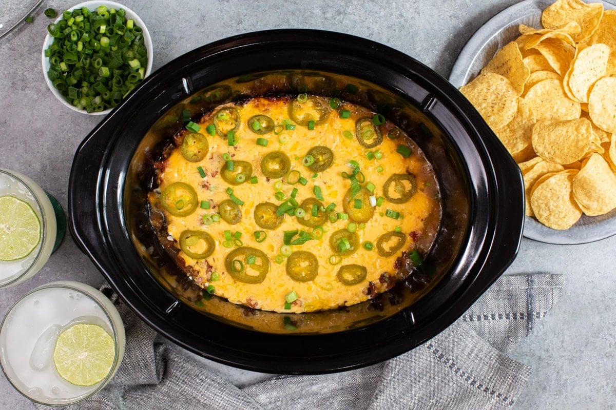 7 layer bean dip done cooking in slow cooker with jalepenos and onions on top.