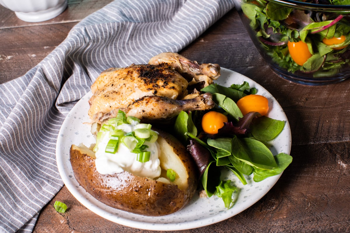 plated Cornish game hen and loaded baked potato on a plate.