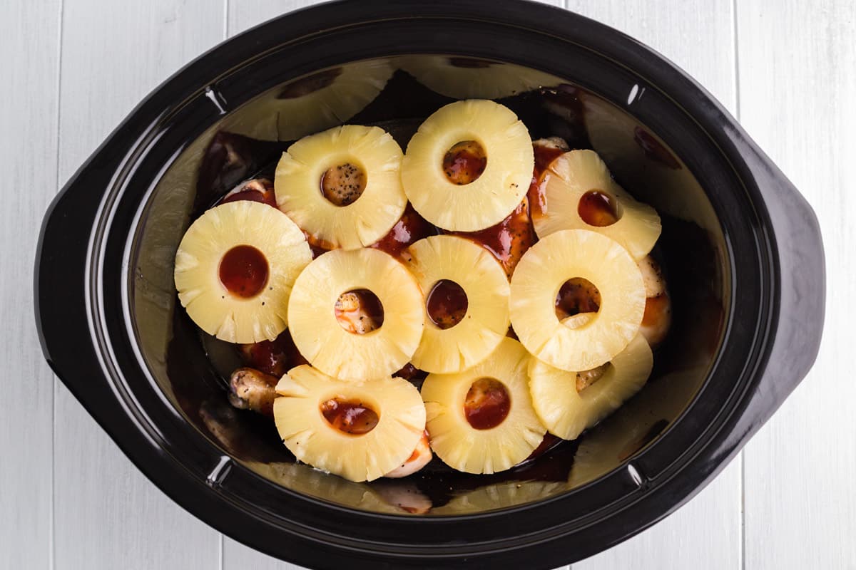 Pineapple rings on top of chicken and bbq sauce in slow cooker