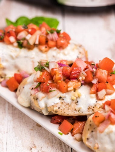 3 chicken breasts on a plate with bruschetta tomato topping and cheese