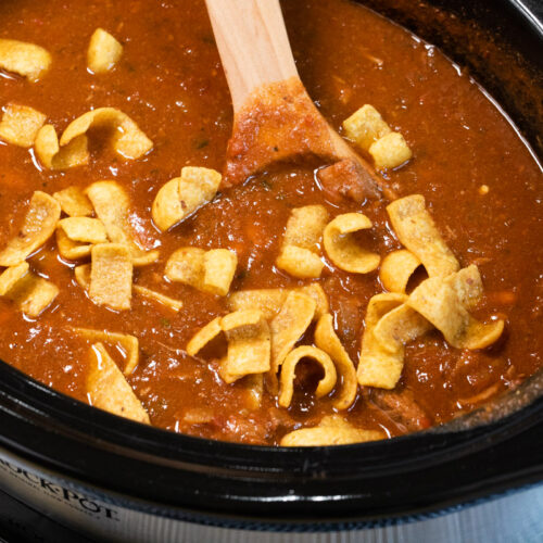 side view of steakhouse style chili in slow cooker with frito chips on top