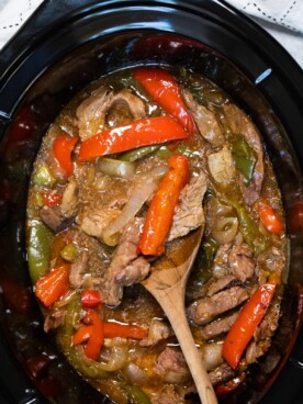 pepper steak in slow cooker with wooden spoon in it.