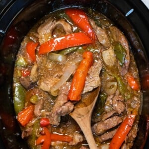 pepper steak in slow cooker with wooden spoon in it.